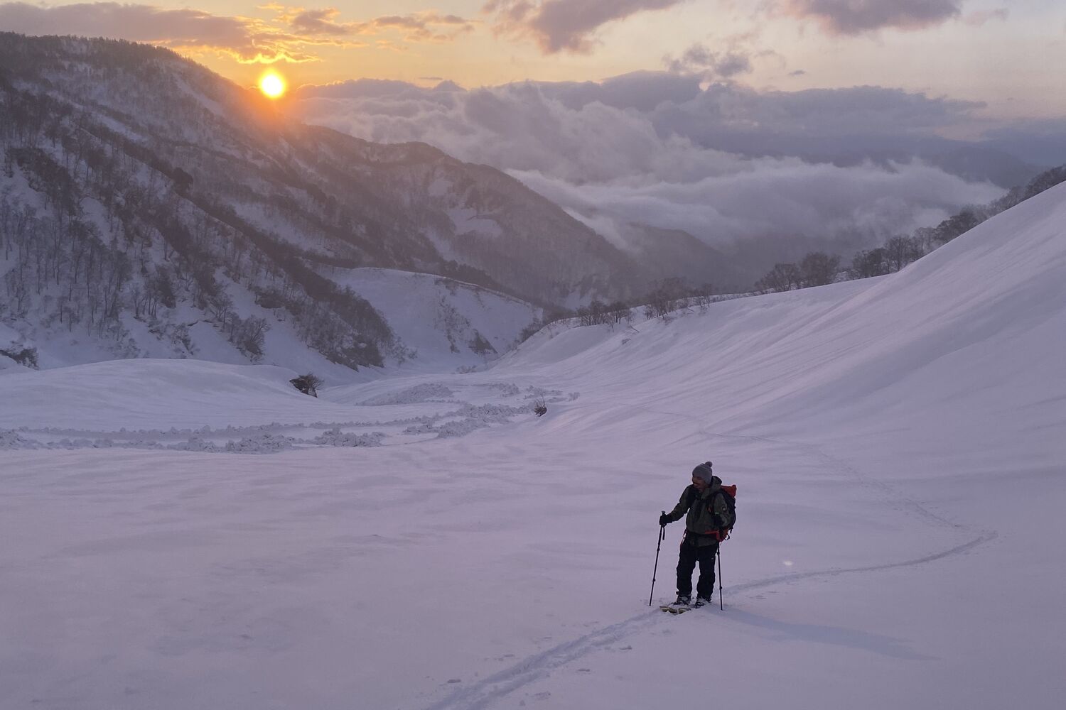 Backcountry splitboarder skinning toward a golden-hour sunrise above a sea of clouds, Japan