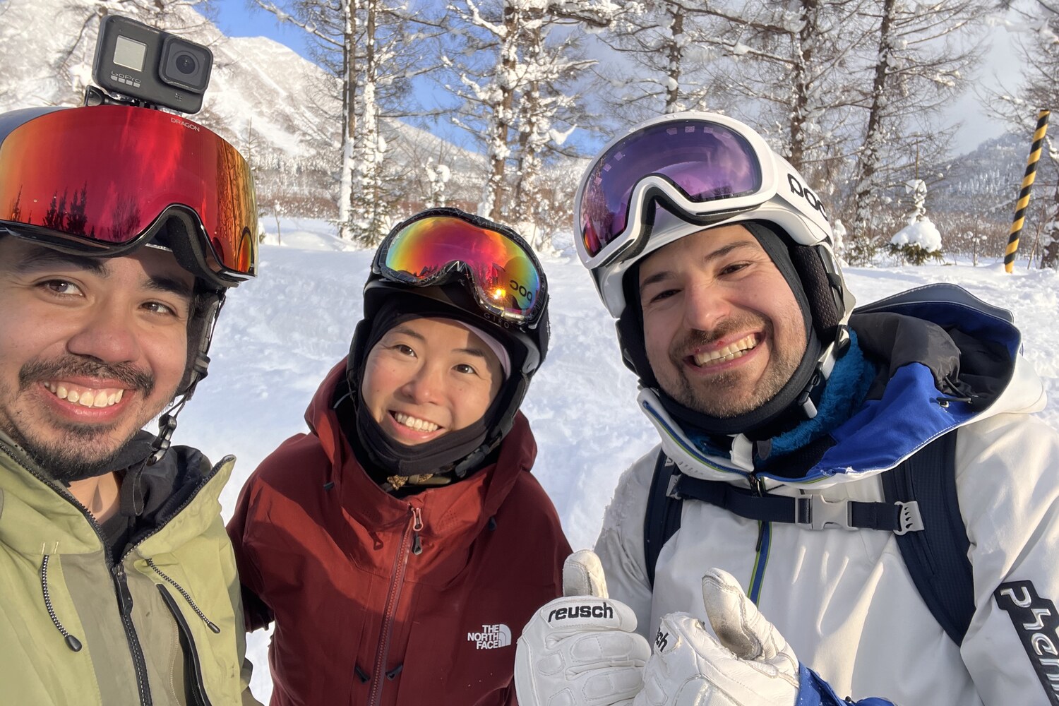 The guide and two happy clients smiling together in the Japan backcountry on a bright winter day