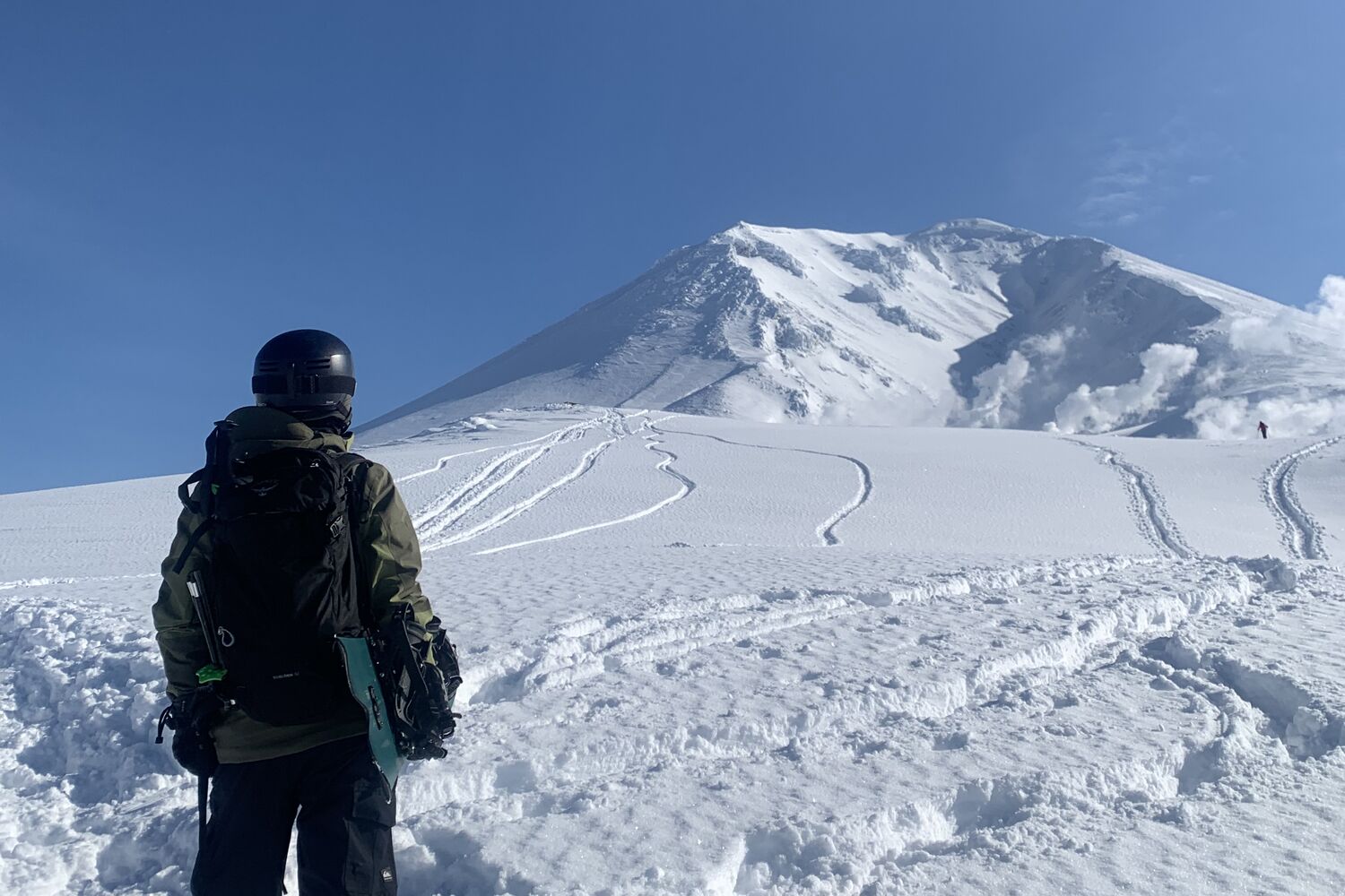 A backcountry tourer gazing up at the volcanic cone of Asahidake, Daisetsuzan, with fresh tracks down the face