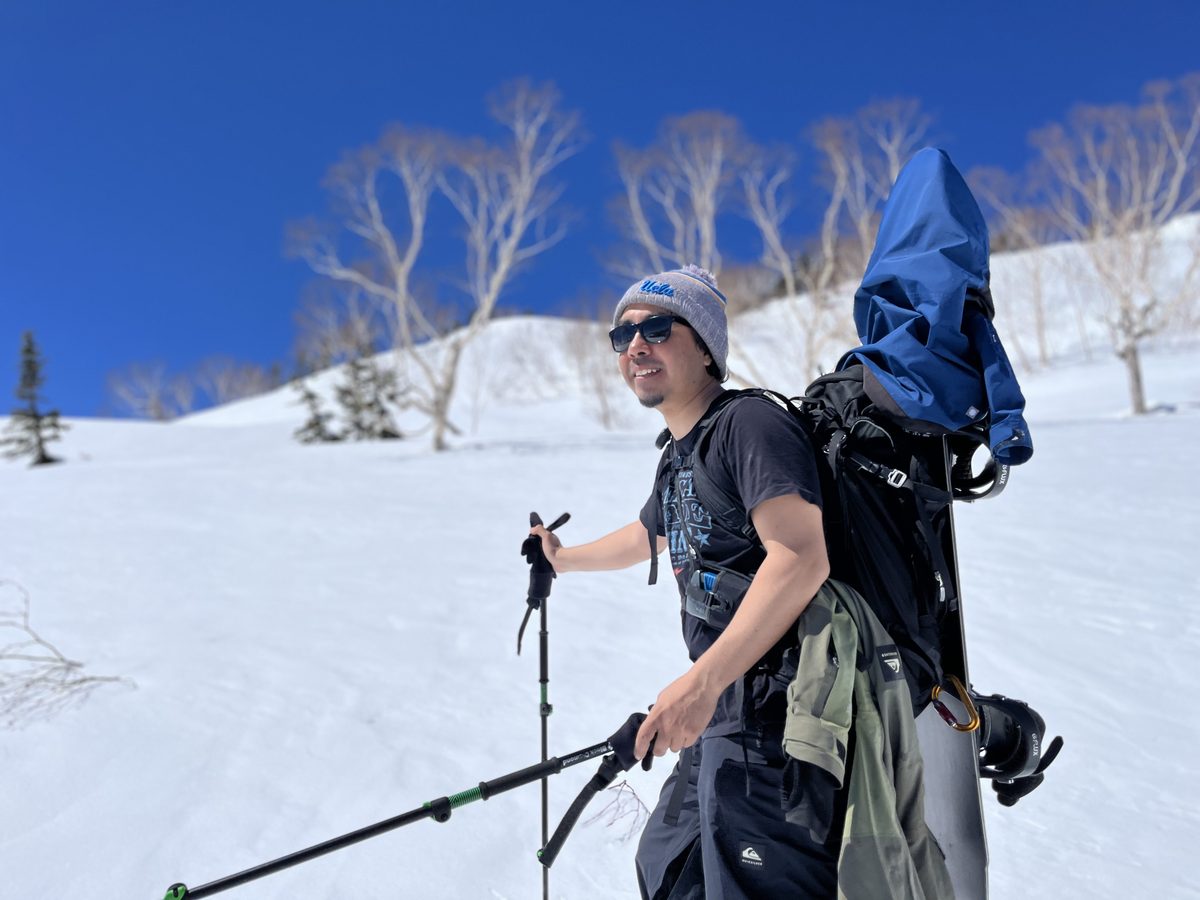 Rick, your guide, touring up a sunlit spring slope with his snowboard on his pack, Japan backcountry