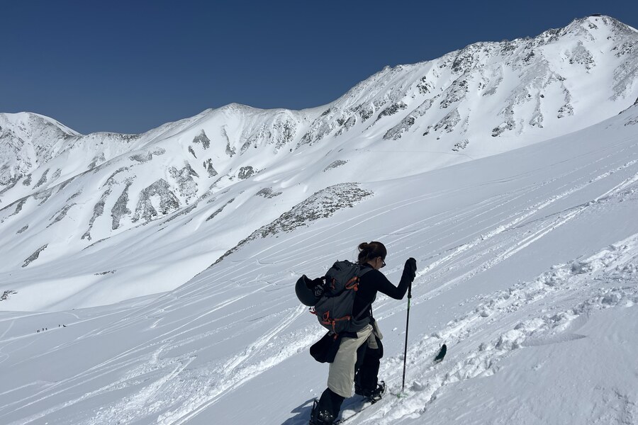 Splitboarder skinning into the bluebird alpine bowl of Tateyama with the peaks behind