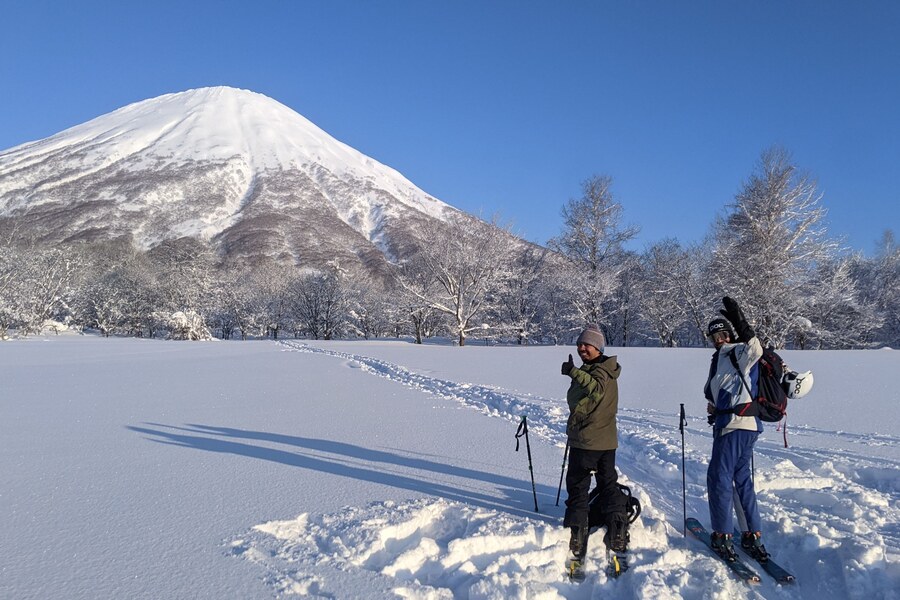 The symmetrical snow-capped cone of Mt Yotei, the Fuji of Hokkaido, with a splitboarder and a skier skinning toward it